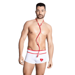 This image features a man modeling a Itspleazure white and red doctor-themed brief roleplay costume. The costume includes a pair of white briefs with a bold red trim and a prominent red heart emblem on the front, paired with a matching red stethoscope.